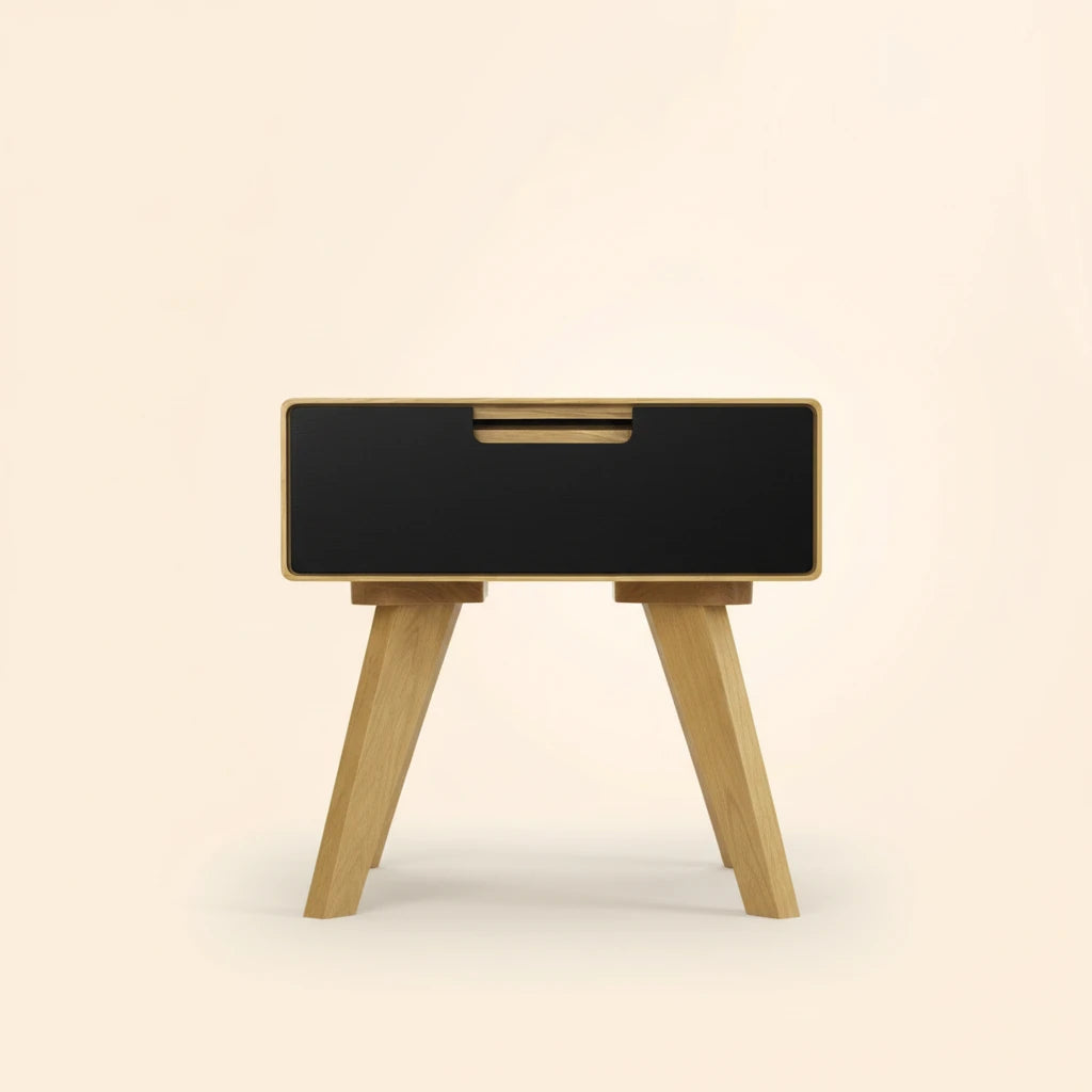 An elegant natural wood side table with a black drawer, centered on a solid #fff2e3 background with soft studio lighting and shadows.