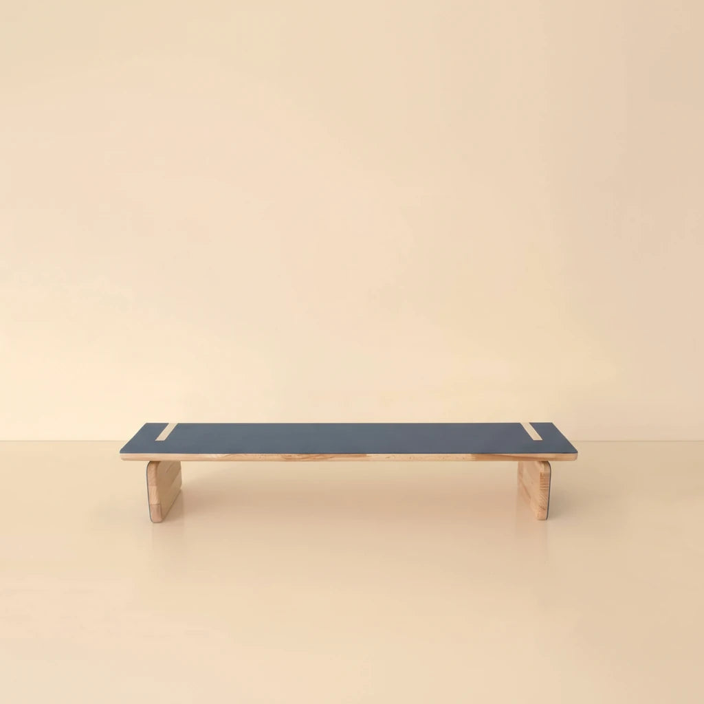 A professional studio photograph of an elegant natural wood bench with a blue top, centered against a light beige background with soft studio lighting and subtle shadows.