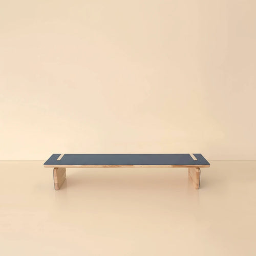 A professional studio photograph of an elegant natural wood bench with a blue top, centered against a light beige background with soft studio lighting and subtle shadows.