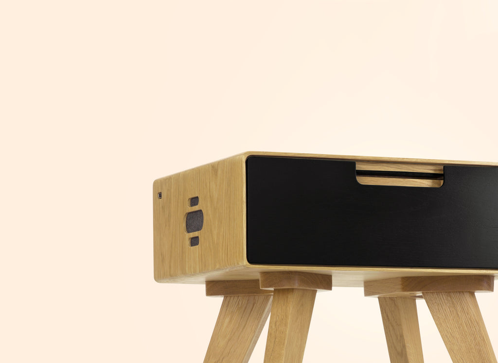 Close-up of natural oak side table with black drawer front and rounded edges