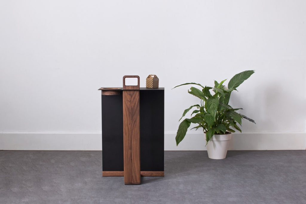Front view of walnut side table with black surface and natural wood details against white wall