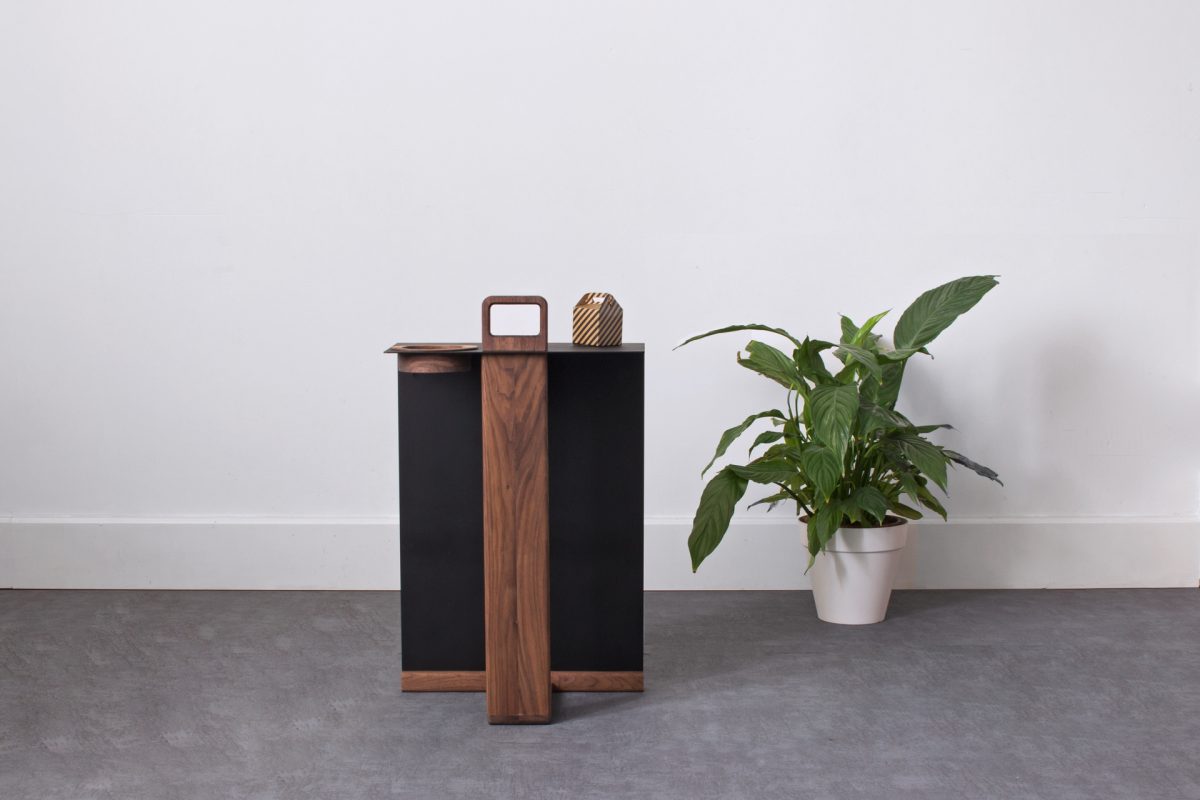 Front view of walnut side table with black surface and natural wood details against white wall
