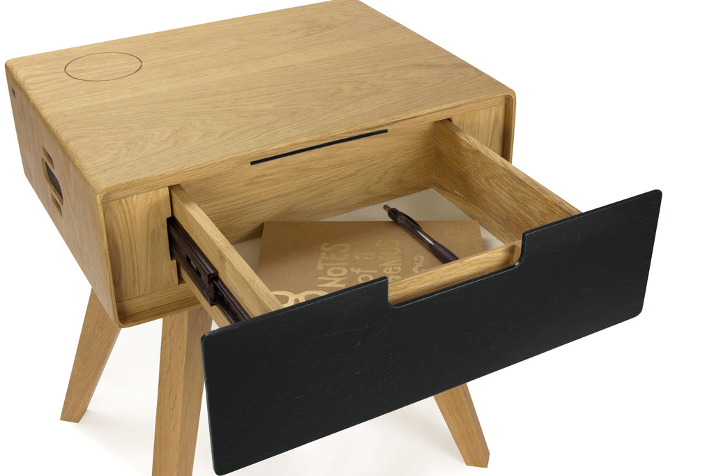 Open drawer of natural oak side table holding a notebook and pen, showing interior storage space